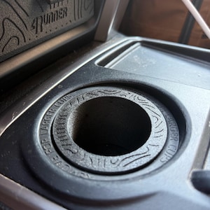 Könnte beinhalten: Schwarzer Kunststoff-Getränkehalter für Autos mit dem Text "FOR LARGER CUPS" am Rand. Der Getränkehalter ist Teil der Innenkonsole eines Autos, im Hintergrund ist das Wort "4Runner" zu sehen.