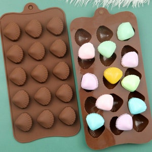 May include: Two brown silicone moulds for making chocolate or candy in the shape of seashells. One mould has 18 individual seashells and the other has 12. The mould on the right has colourful candies in the seashells.