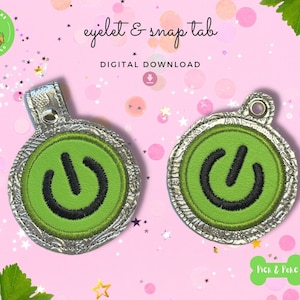 May include: Two round, silver-colored, embroidered patches with a green power button symbol. The patches have an eyelet and snap tab for attaching to a bag or other item. The text "eyelet & snap tab" and "DIGITAL DOWNLOAD" is visible above the patches.