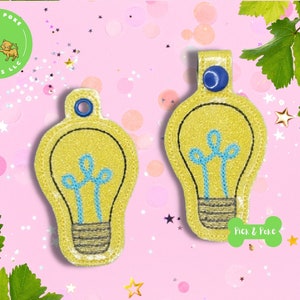 May include: Two yellow lightbulb-shaped keychains with blue filament details. The keychains are embroidered with a black outline and have a blue button on the top.