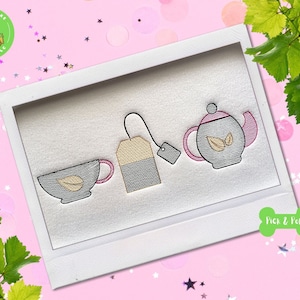 May include: A white embroidery design of a teacup, teapot, and tea bag on a white background. The teacup and teapot have a gray outline and a light brown interior. The tea bag is gray with a light brown tag. The design is framed in a white frame.