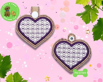Puede incluir: Dos llaveros en forma de corazón de color morado y blanco con respaldo de corcho. Los llaveros tienen un botón blanco en la parte superior y están sobre un fondo rosa con estrellas blancas.