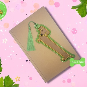 May include: A green and brown dachshund bookmark with a green tassel. The bookmark is on a brown notebook with the text "Pick & Poke" on a green bone shape.