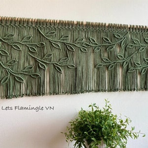 May include: A green macrame wall hanging with a leaf design. The hanging is made with thick cotton cord and has a wooden dowel at the top. The text "Lets Flamingle VN" is visible at the bottom of the image.