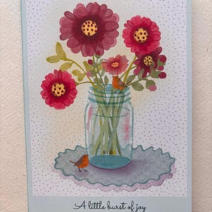 May include: A greeting card featuring a watercolor illustration of a clear glass mason jar filled with dark pink flowers and green stems. Two small orange birds are depicted, one perched on the stems and one on a scalloped mat. Text reads: A little burst of joy.
