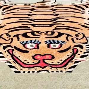 K&ouml;nnte beinhalten: Ein gro&szlig;er Tigerteppich mit gr&uuml;nem Hintergrund. Der Tiger ist braun und schwarz mit einer rosa Nase und einem rosa Maul. Der Teppich hat einen wei&szlig;en Rand und der Text "HYPECULTURE CO" befindet sich in der linken unteren Ecke.