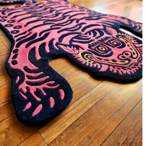 May include: A pink and black tiger rug with a gold outline. The rug is made of a soft, plush material and has a detailed design.