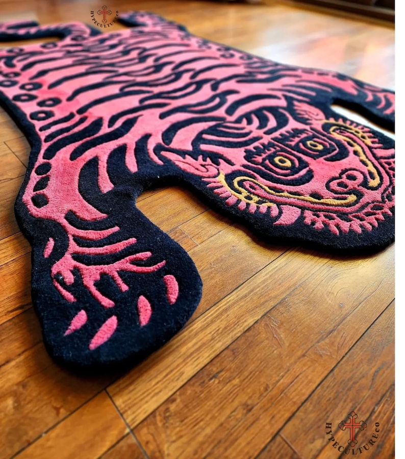 May include: A pink and black tiger rug with a gold outline. The rug is made of a soft, plush material and has a detailed design.