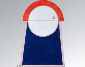 Puede incluir: Una alfombra geométrica azul y naranja con un círculo blanco en el centro. La alfombra tiene un borde rosa y un pequeño logotipo de cruz en la esquina superior derecha.