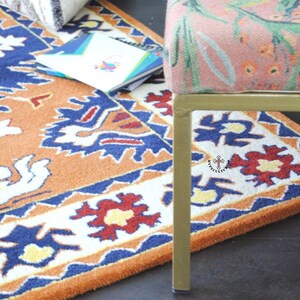 May include: A close-up of a colorful rug with a geometric pattern in shades of orange, blue, white, and red. The rug is partially covered by a gold metal chair with a floral patterned fabric seat.