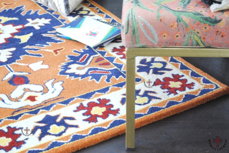 May include: A close-up of a colorful rug with a geometric pattern in shades of orange, blue, white, and red. The rug is partially covered by a gold metal chair with a floral patterned fabric seat.