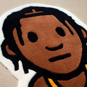 May include: A brown and black rug with a cartoon-style illustration of a person with brown skin, black hair, and a yellow necklace. The person is smiling and has a simple, cartoon-style face.