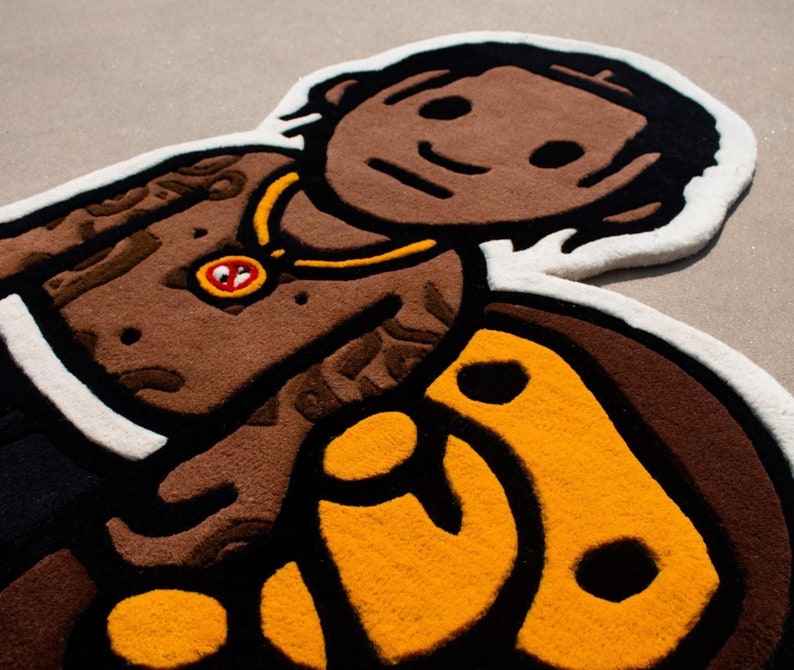 May include: A brown and yellow rug with a cartoon-like image of a person with a gold chain and a black and yellow design. The rug is made of a soft, plush material.