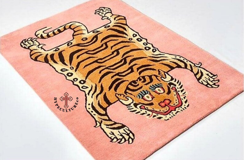 K&ouml;nnte beinhalten: Ein rosa Teppich mit einem Tigerdesign. Der Tiger liegt auf dem R&uuml;cken mit seinen Pfoten in der Luft. Der Teppich tr&auml;gt den Text "Hypecultureco" in der linken unteren Ecke.