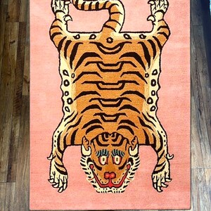 K&ouml;nnte beinhalten: Ein rosa Teppich mit einem Tigermuster. Der Tiger liegt auf dem R&uuml;cken mit seinen Pfoten in der Luft. Der Tiger ist braun und schwarz mit einem wei&szlig;en Gesicht. Der Teppich ist aus Wolle.