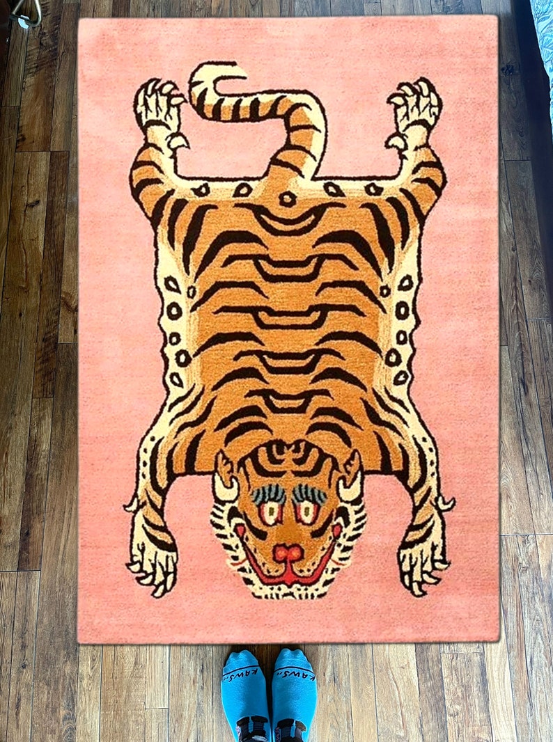 K&ouml;nnte beinhalten: Ein rosa Teppich mit einem Tigermuster. Der Tiger liegt auf dem R&uuml;cken mit seinen Pfoten in der Luft. Der Tiger ist braun und schwarz mit einem wei&szlig;en Gesicht. Der Teppich ist aus Wolle.