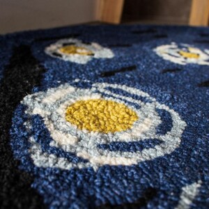 May include: Close-up of a blue rug with a white and yellow circular pattern. The rug is made of a soft, fluffy material.