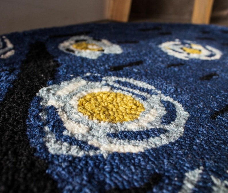 May include: Close-up of a blue rug with a white and yellow circular pattern. The rug is made of a soft, fluffy material.