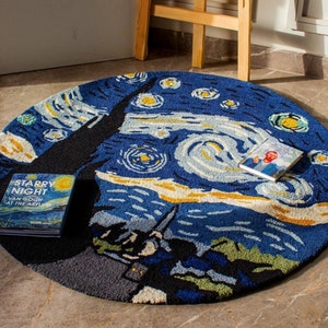 May include: A round rug with a blue and yellow design inspired by Vincent van Gogh's "Starry Night" painting. The rug features swirling lines and stars, and the text "Starry Night" is visible on a book lying on the rug.
