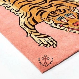 K&ouml;nnte beinhalten: Ein rosa Teppich mit einem Tigerdesign. Der Tiger ist braun und schwarz mit wei&szlig;em Hintergrund. Der Teppich tr&auml;gt den Text "HyppeCultureCo" in schwarzen Buchstaben.