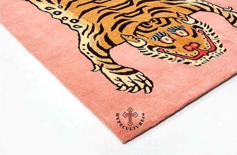 K&ouml;nnte beinhalten: Ein rosa Teppich mit einem Tigerdesign. Der Tiger ist braun und schwarz mit wei&szlig;em Hintergrund. Der Teppich tr&auml;gt den Text "HyppeCultureCo" in schwarzen Buchstaben.