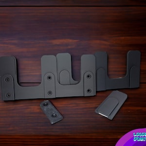 Peut inclure: Quatre supports en métal noir avec des trous de vis, conçus pour le montage d'étagères ou d'autres objets. Les supports sont disposés en rangée sur une surface en bois. Il y a deux autres supports plus petits sur la surface.