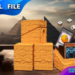 Puede incluir: Una caja de juego de cartas impresa en 3D, de color naranja, con temática egipcia, con una ranura para cartas y dados. La caja está compuesta por cuatro piezas que encajan entre sí. La caja está colocada sobre una mesa de madera con una ventana en el fondo que muestra un paisaje desértico con pirámides.