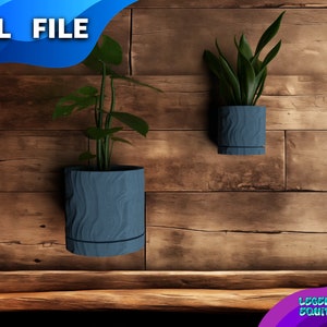 Op de afbeelding: Twee blauwe keramische potten met een houtnerfstructuur, hangend aan een houten muur. De potten zijn leeg en klaar om met planten te worden gevuld.  .STL FILE