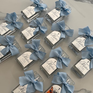 May include: A collection of rectangular glass spray bottles, each topped with a light blue fabric bow. The labels feature a cross icon, the text "BAPTISM OF Mateo", the name "OCAMPO", the date "25.10.2026", and the scent "LYCHEE PEONY ROOM SPRAY".