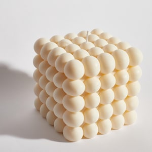 May include: A white square candle with a textured surface made of small, round bumps.