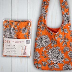 May include: A DIY reversible hobo bag sewing kit in a clear plastic package next to a finished hobo bag. Both feature an orange fabric with a black and white floral pattern. The kit label lists contents including 2 yards of fabric.