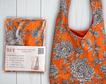 May include: A DIY reversible hobo bag sewing kit in a clear plastic package next to a finished hobo bag. Both feature an orange fabric with a black and white floral pattern. The kit label lists contents including 2 yards of fabric.