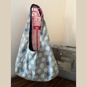May include: A light gray tote bag with a floral pattern of white and blue flowers. The bag has a navy blue polka dot lining and a wide strap. A pink wire dress form is inside the bag. A Singer sewing machine is in the background.