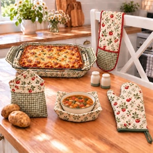 May include: A rectangular glass baking dish filled with lasagna, a fabric bowl cozy holding a bowl of soup, a matching fabric oven mitt, a hanging oven mitt, and two salt and pepper shakers. The fabric items feature a red tomato and green leaf print.