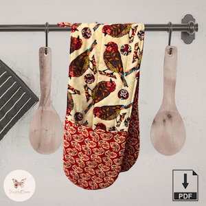May include: A colorful oven mitt with a bird pattern in red, brown, and orange on a cream background. The bottom portion features a red paisley design. The mitt hangs on a metal rod with wooden spoons on either side, suggesting a kitchen setting.
