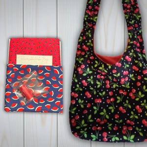 May include: A hobo bag with a black fabric featuring a red cherry and white polka dot pattern, alongside a folded fabric kit with a red watermelon seed pattern and a blue watermelon slice pattern, including a small spool of red thread.
