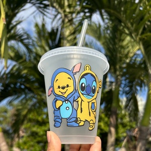 May include: A clear plastic tumbler with a straw, featuring a cartoon image of Stitch and a baby Winnie the Pooh. The characters are wearing blue and yellow outfits.