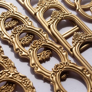 May include: Close-up of several ornate, gold-colored decorative frames. The frames have an oval center and are embellished with intricate floral and scrollwork designs. The frames are arranged in a diagonal pattern.