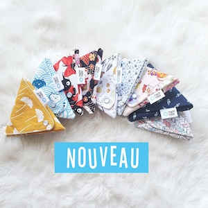Peut inclure: Une collection de neuf pochettes en tissu triangulaires colorées avec une variété de motifs, y compris des imprimés floraux, géométriques et animaliers. Les pochettes sont disposées en demi-cercle et portent un logo circulaire bleu avec le texte "Pinchy Pouch" sur chacune. Le texte "NOUVEAU" est affiché en lettres bleues sous les pochettes.