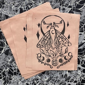May include: A stack of brown paper prints featuring a black and white illustration of a moth with wings spread wide. The moth is surrounded by a crescent moon, stars, and a floral design.