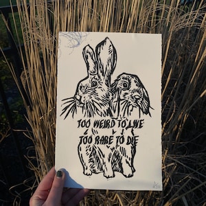 Peut inclure: Gravure sur linoléum en noir et blanc de deux lapins avec le texte "Trop bizarre pour vivre, trop rare pour mourir".