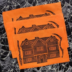 May include: Four orange prints of a black and white illustration of a house with a broom and a scythe. The house has a pointed roof and three windows on each side. The house is on a black and white background.
