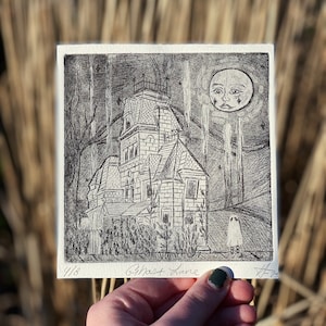 May include: A black and white linocut print of a spooky house with a ghost in front of it. The moon is a face with a tear running down its cheek. The print is titled "Ghost Lane" and numbered 4/8.
