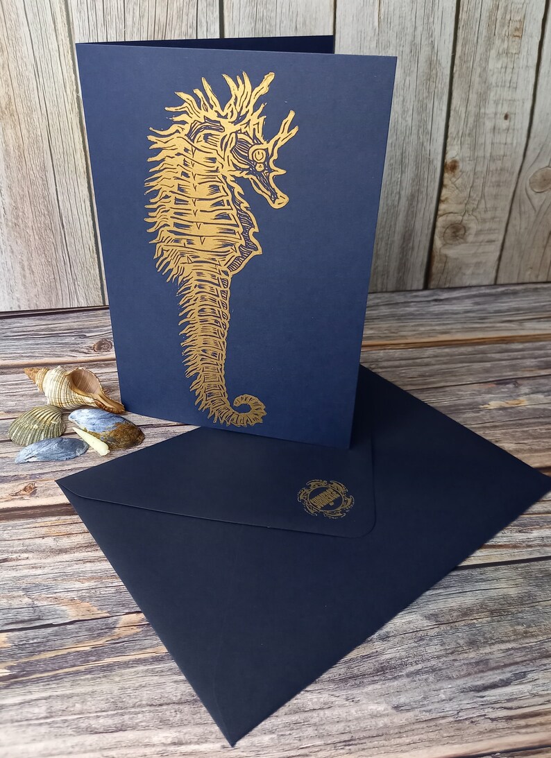 May include: A navy blue card with a gold foil embossed seahorse design. The card is blank inside and comes with a matching navy blue envelope.