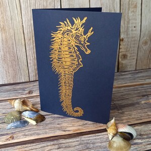 May include: A navy blue card with a gold foil seahorse illustration. The seahorse is detailed and intricate, with a textured appearance.
