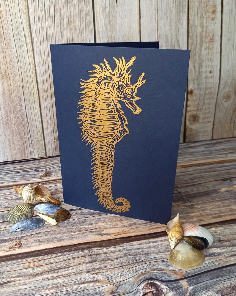 May include: A navy blue card with a gold foil seahorse illustration. The seahorse is detailed and intricate, with a textured appearance.
