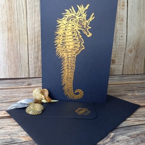 May include: A gold foil seahorse illustration on a black card with a matching black envelope. The seahorse is detailed and intricate.