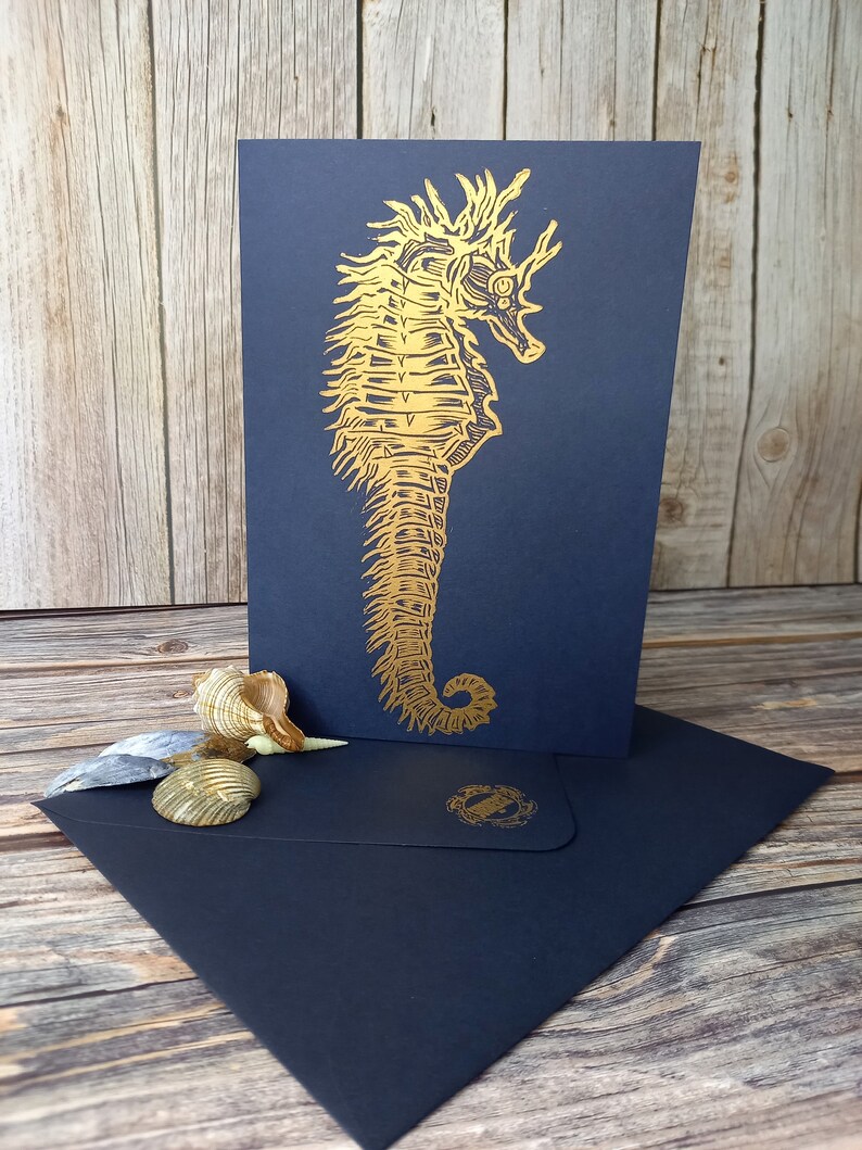 May include: A gold foil seahorse illustration on a black card with a matching black envelope. The seahorse is detailed and intricate.