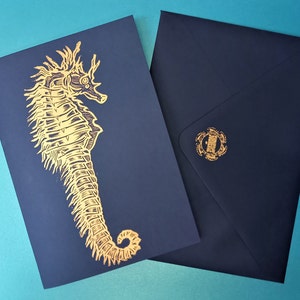 May include: A navy blue card with a gold foil seahorse design. The card is blank inside and comes with a matching navy blue envelope.