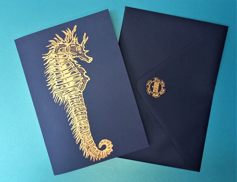 May include: A navy blue card with a gold foil seahorse design. The card is blank inside and comes with a matching navy blue envelope.